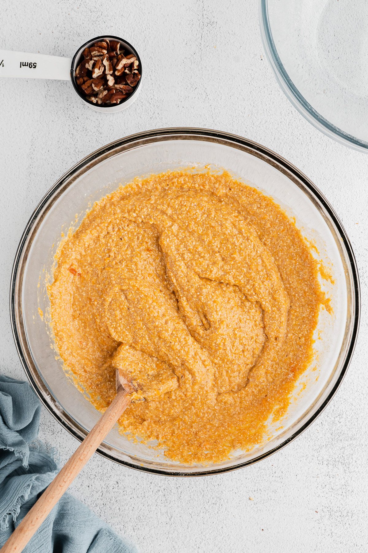 Batter for sweet potato muffins in a clear bowl on a white background with pecans on the side