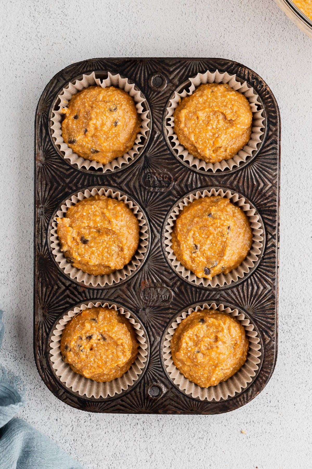 an overhead shot of a 6 muffin tin with paper liners and uncooked batter in each spot