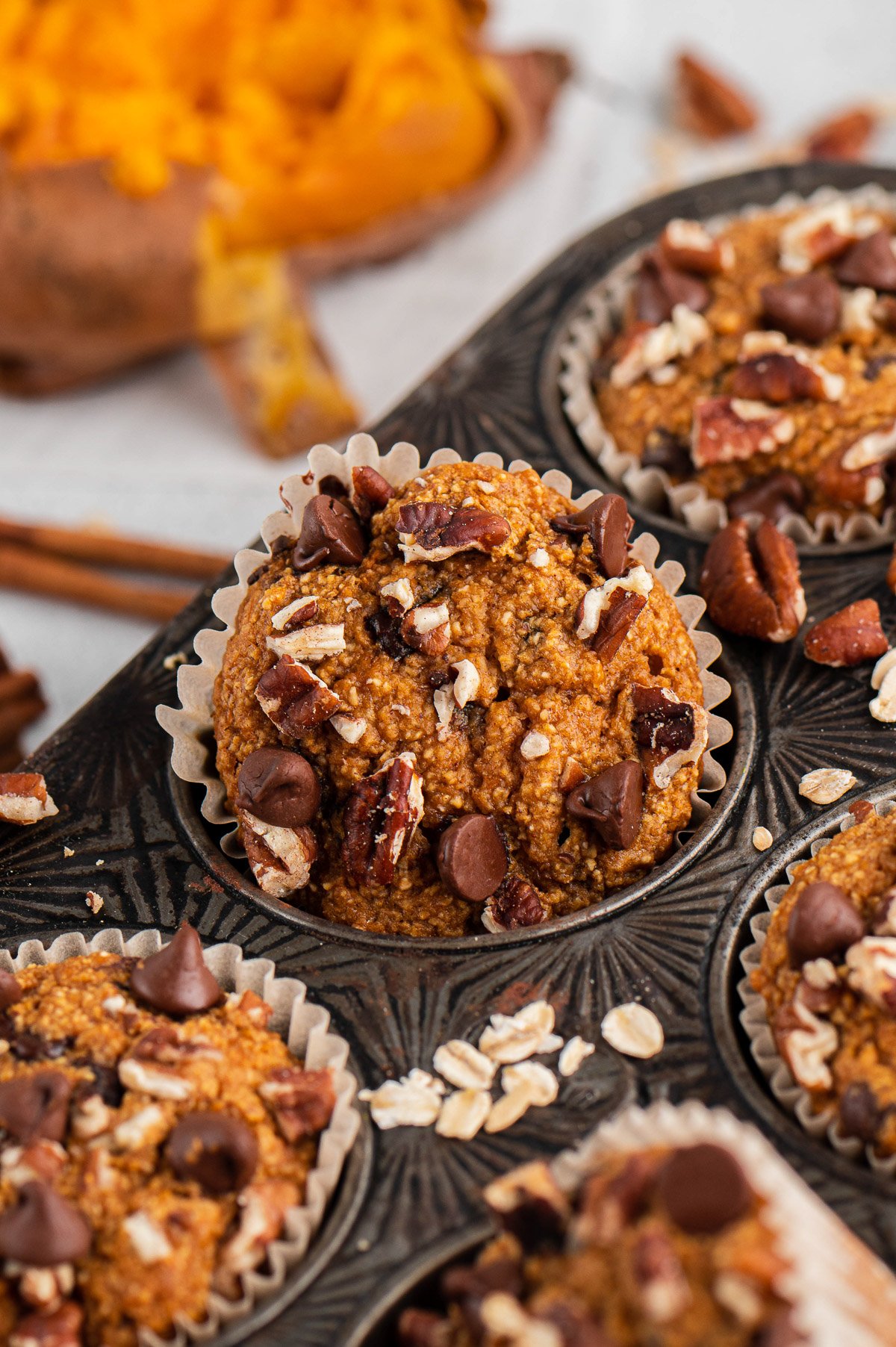 A sweet potato muffin getting taken out of a muffin tin on a white background
