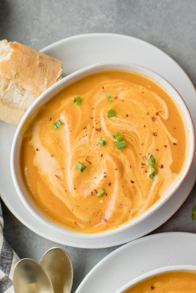 A bowl of Sweet Potato Soup on a white plate with bread off to the side