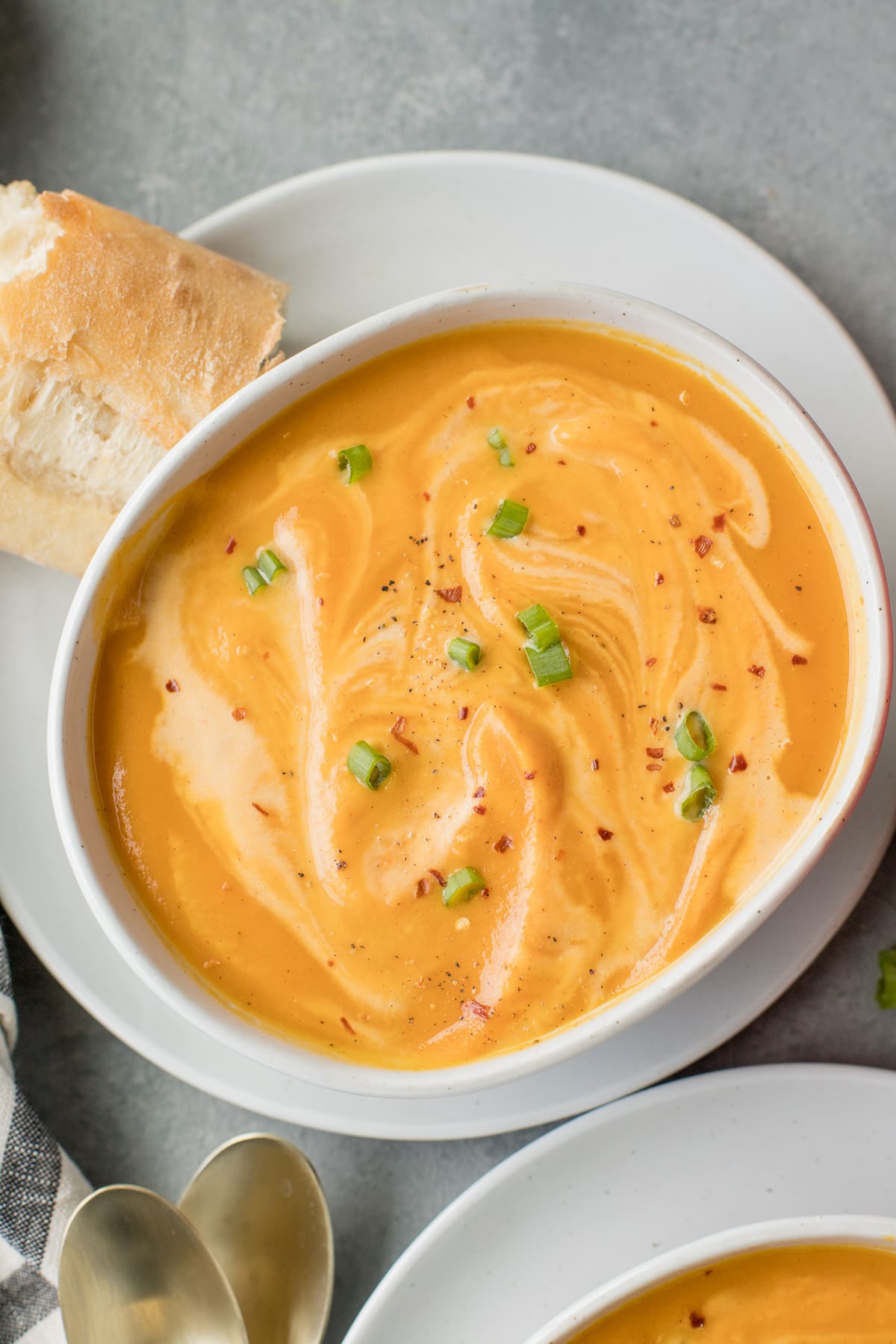 A bowl of Sweet Potato Soup on a white plate with bread off to the side