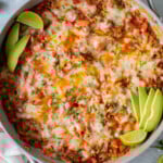 An overhead shot of a taco skillet in a large pan garnished with avocado slices and lime wedges on a grey background