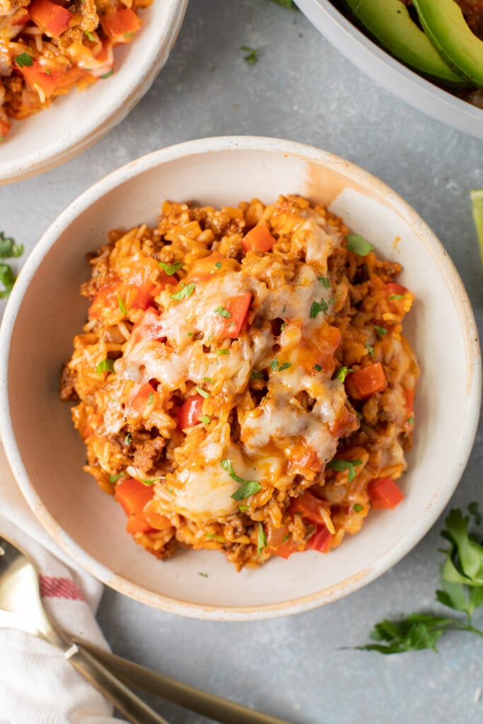 A close up of a serving of cheesy taco skillet on a white plate with another white plate on the side on a grey background