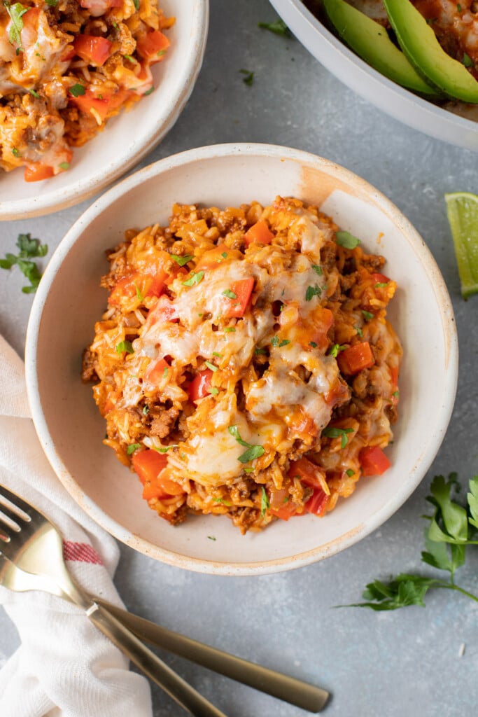 A serving of cheesy taco skillet on a white plate with another white plate on the side on a grey background