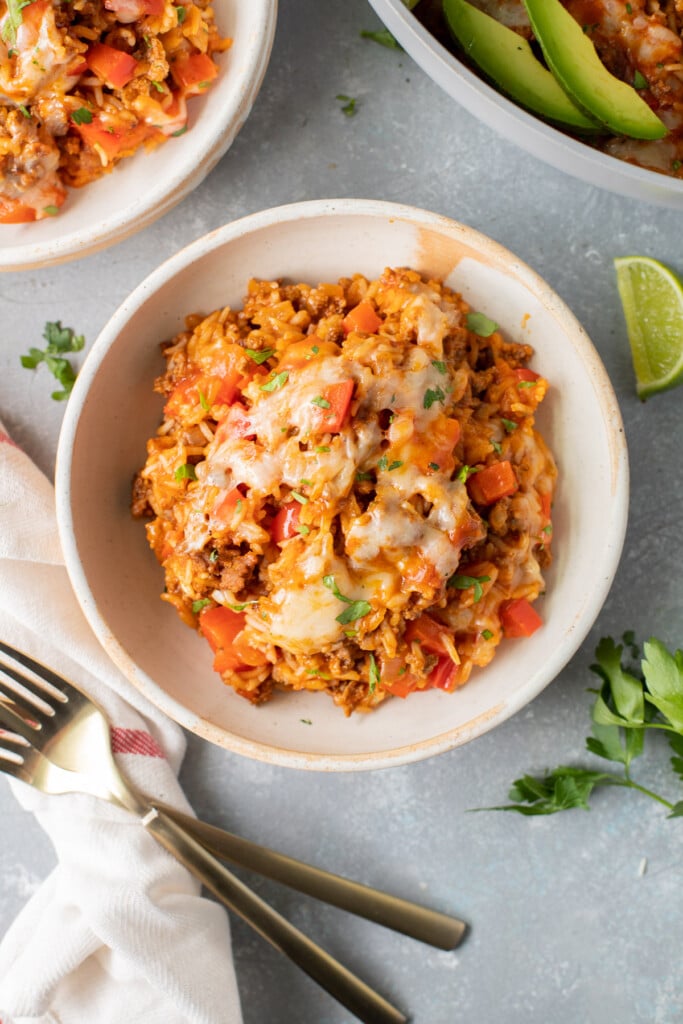 A serving of cheesy taco skillet on a white plate with another white plate on the side on a grey background