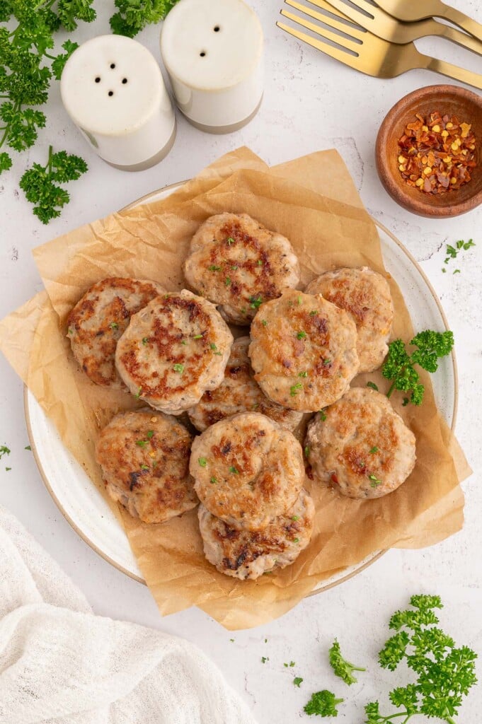 An overhead shot of Turkey Breakfast Sausage patties on a piece of parchment paper on a white plate.
