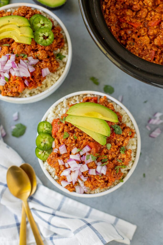A close up of two bowls of healthy turkey chili on a grey background with a crockpot