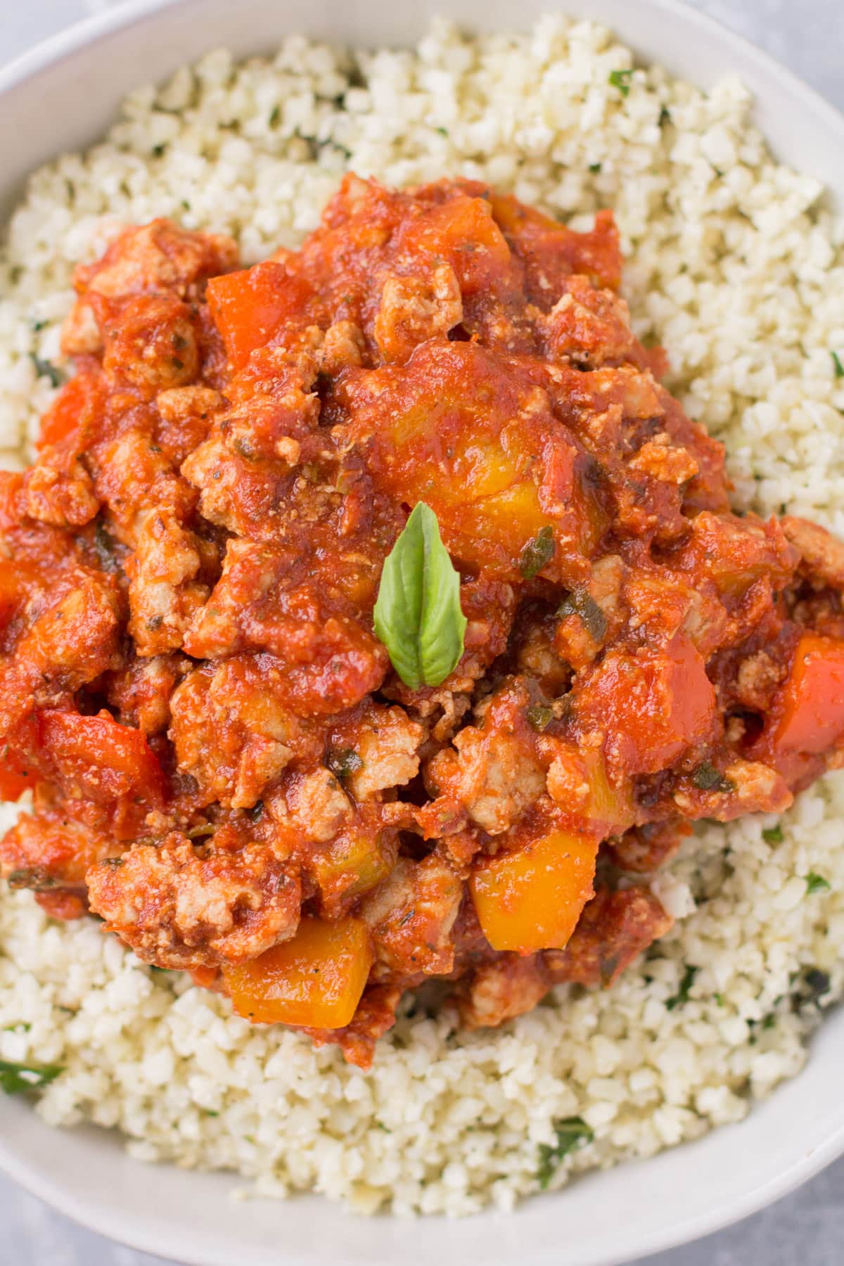A close up of Healthy Unstuffed Peppers in a white bowl. Ground meat + peppers in a sauce over cauliflower rice.