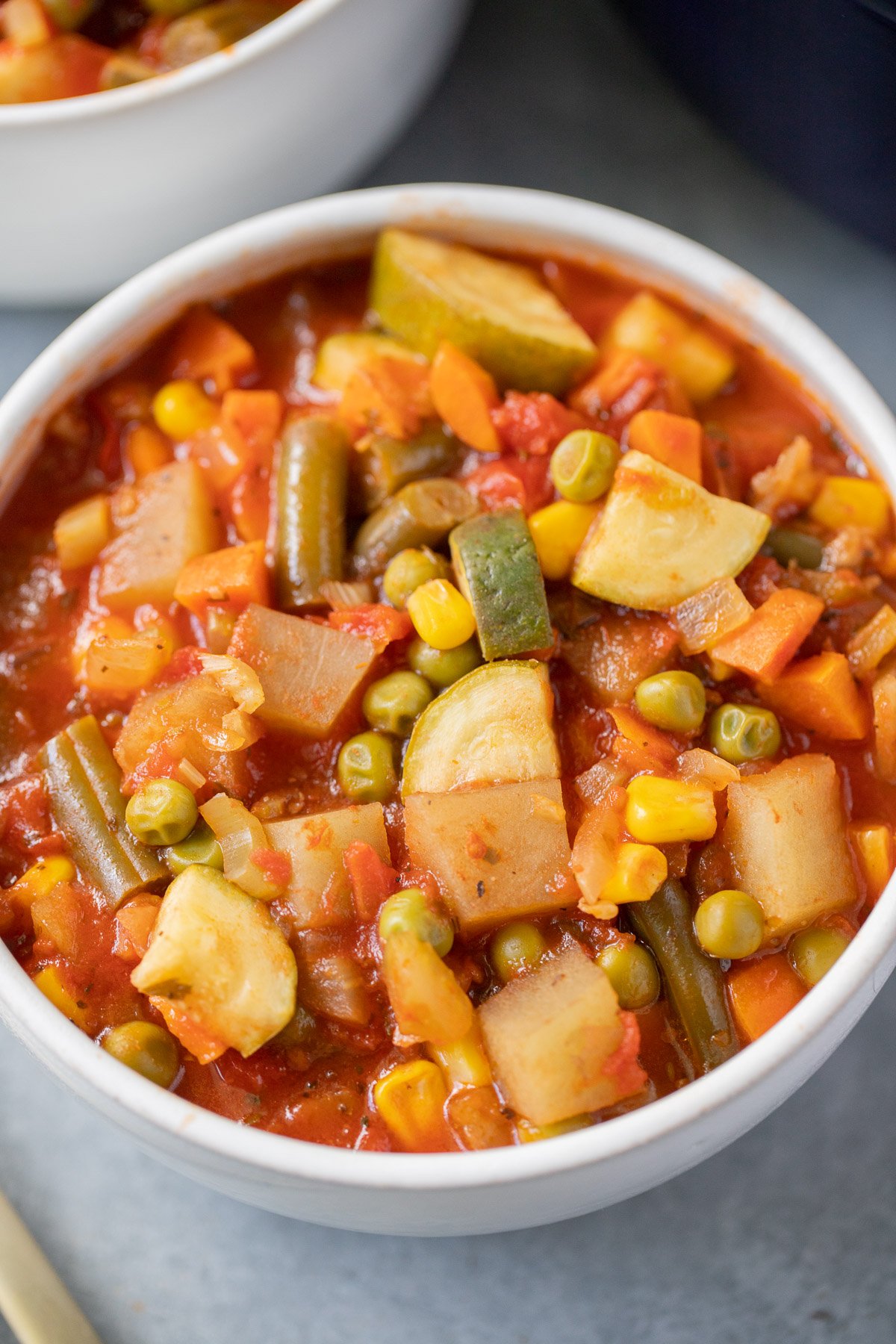 A white bowl of homemade vegetable soup on a grey background