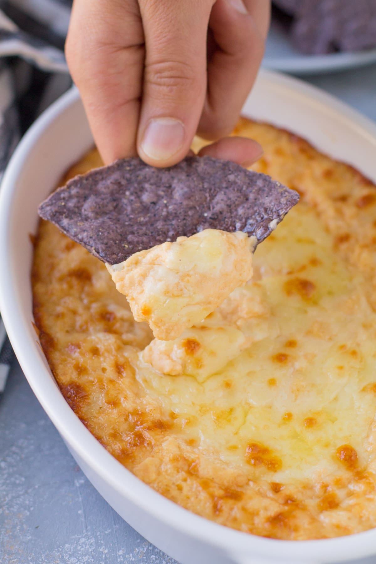 A hand scooping a bite ofVegetarian Buffalo Dip out of a white dish with a blue tortilla chip