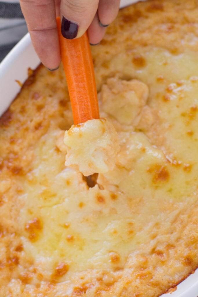 A carrot taking a scoop out of Vegetarian dip with no cream cheese