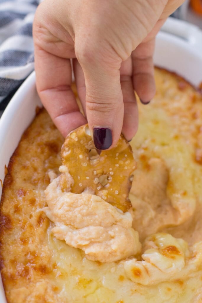 A hand scooping a bite of Vegetarian buffalo bean dip out of a white oval bowl