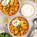 Two bowls of white bean chicken chili in white bowls on a grey background with fresh cilantro and lime wedges on the side.