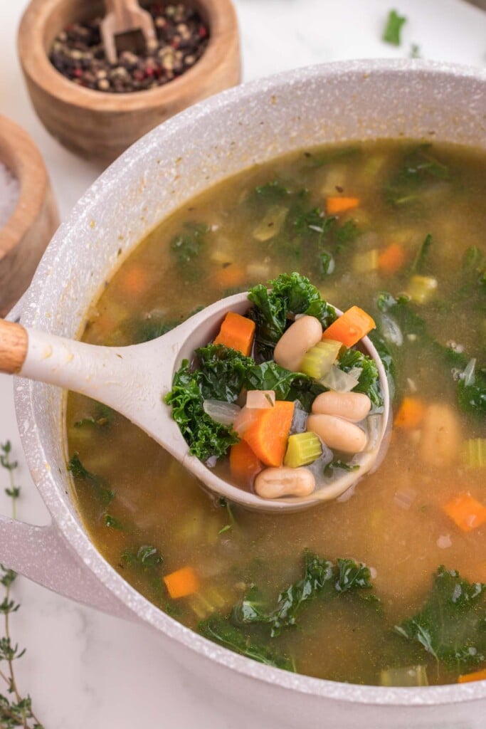 A ladle taking a scoop out of a dutch oven filled with Tuscan white bean soup.