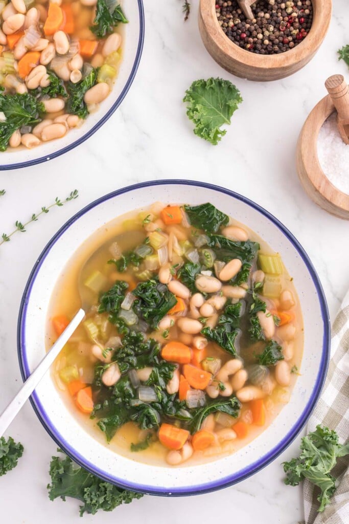 A white and blue rimmed bowl of Tuscan white bean soup on a white counter.