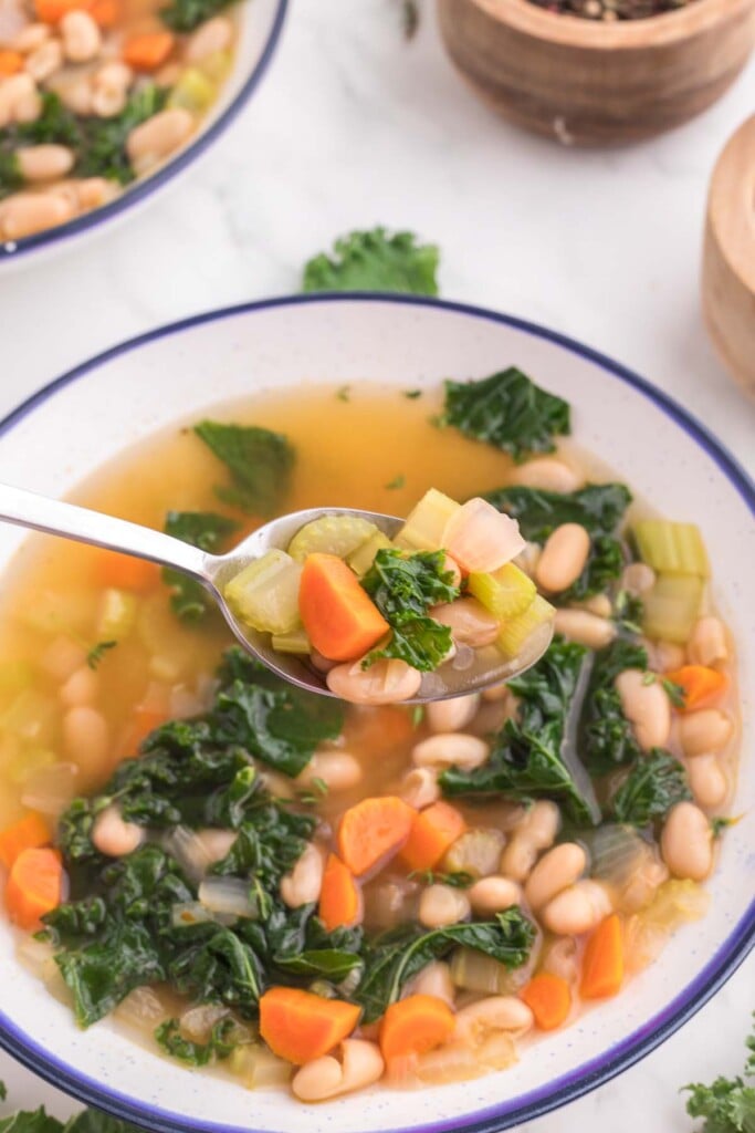 A spoon taking a bite out of a white and blue bowl of Tuscan white bean soup.