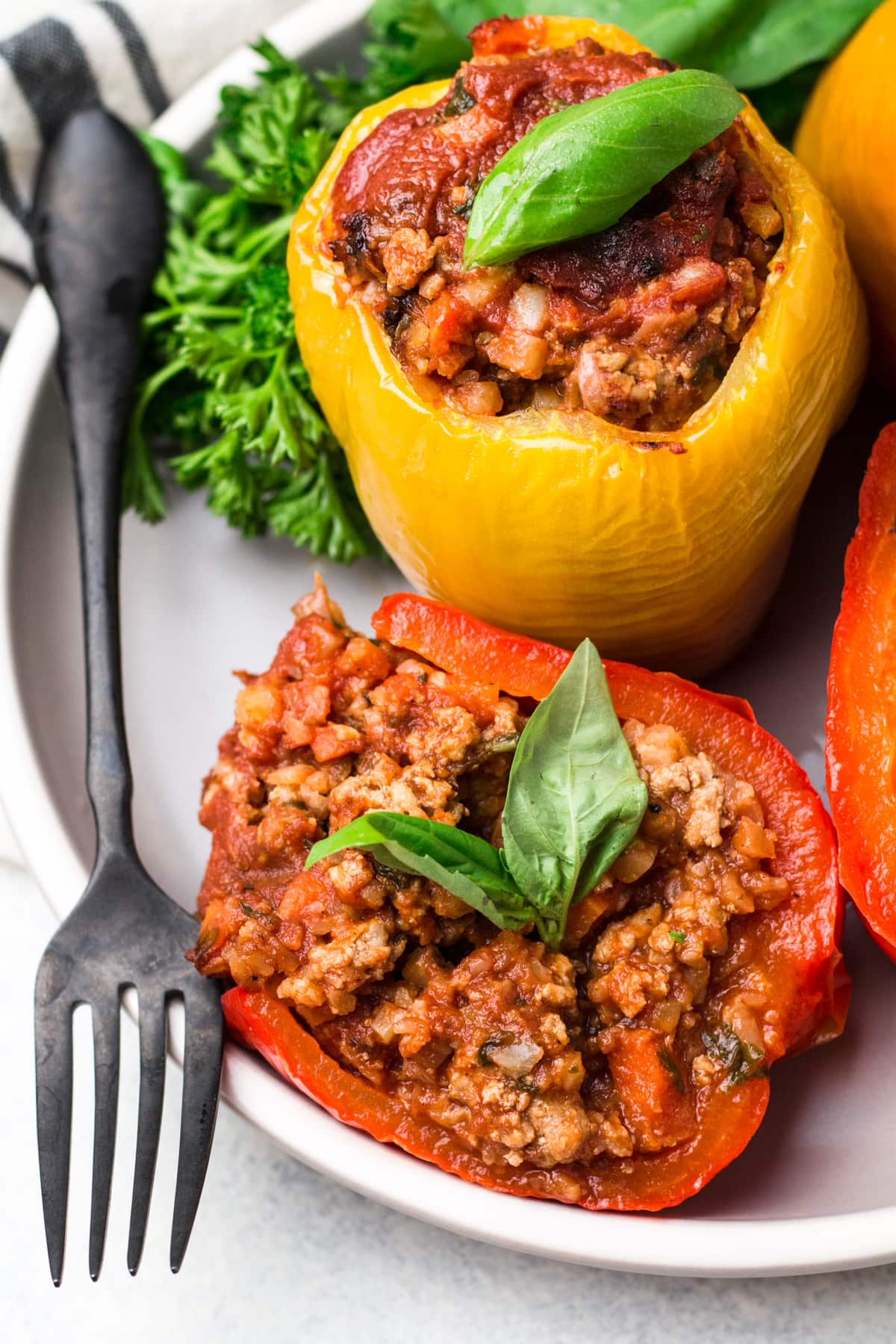 Whole30 stuffed peppers on a white plate with a grey background + green linen in the back.