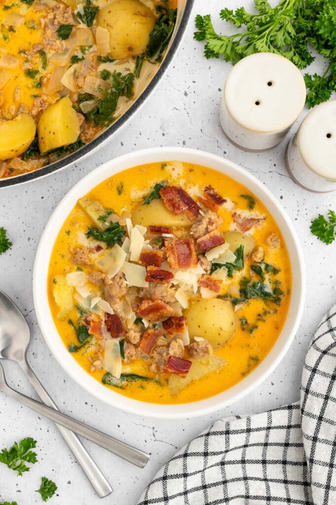 Healthy zuppa toscana in a white bowl with a dutch oven of the soup on the side on a white counter