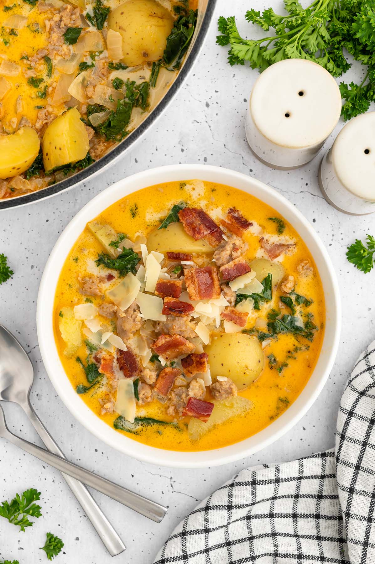 Healthy zuppa toscana in a white bowl with a dutch oven of the soup on the side on a white counter