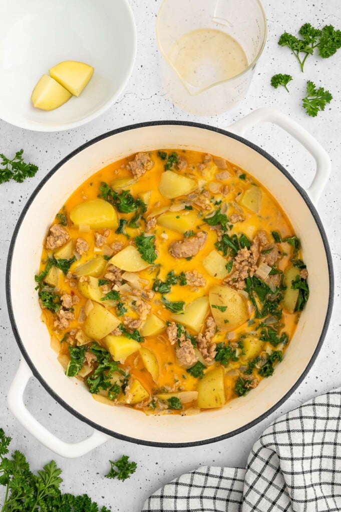 Healthy Zuppa Toscana Soup in a dutch oven on a white counter with more bowls on the side