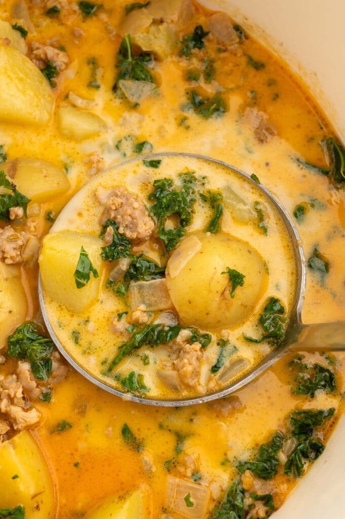 A ladle taking a large scoop of zuppa toscana soup out of a dutch oven of the soup