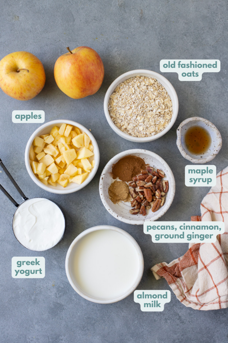 Ingredients for apple pie overnight oats in white bowls: old fashioned rolled oats, nonfat greek yogurt, almond milk, cinnamon, ground ginger, apples, pecans, maple syrup