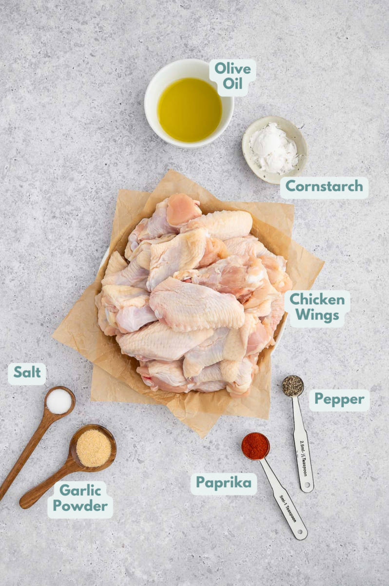 Ingredients for Baked Chicken Wings in small bowls and measuring spoon: chicken wings, olive oil , cornstarch, salt, pepper, paprika, garlic powder