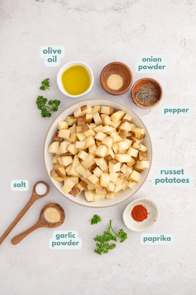 Ingredients for breakfast potatoes in small bowls: russet potatoes, olive oil, salt, pepper, garlic powder, onion powder, paprika