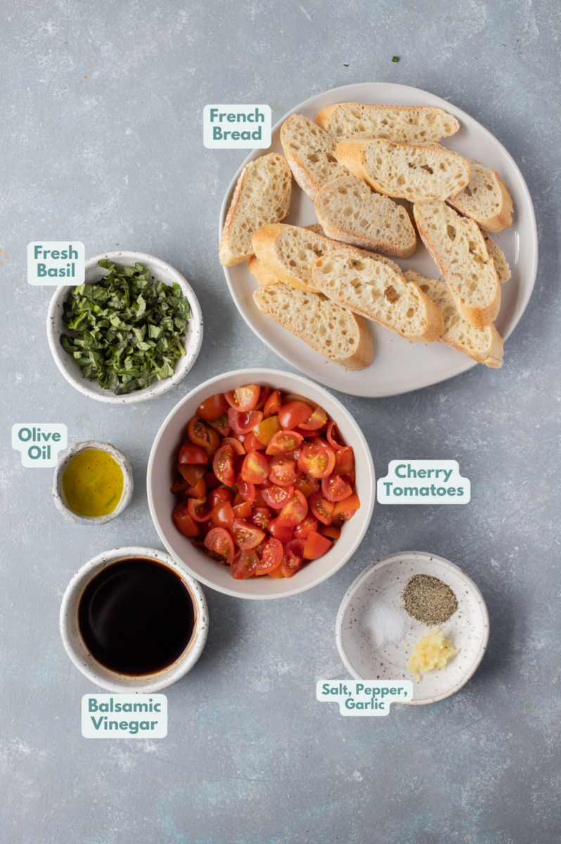 Ingredients for homemade bruschetta in small white bowls: cherry tomatoes, olive oil, balsamic vinegar, garlic, fresh basil, salt, pepper, french bread