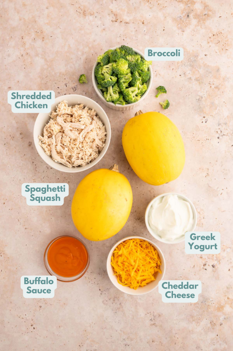 Ingredients for buffalo chicken spaghetti squash in small bowls: spaghetti squash, shredded chicken breasts, broccoli florets, cheddar cheese, buffalo sauce, nonfat greek yogurt