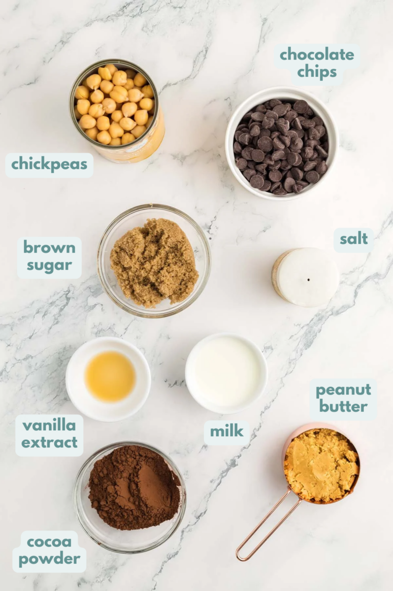 Ingredients for chocolate hummus in small bowls: chickpeas, peanut butter, cocoa powder, brown sugar, milk, vanilla extract, salt, chocolate chips