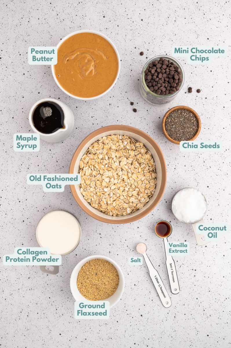 An overhead shot of ingredients for energy balls in small bowls: creamy natural peanut butter, maple syrup, coconut oil, vanilla extract, collagen protein powder, ground flaxseed, old fashioned oats, chia seeds, sea salt, mini chocolate chips