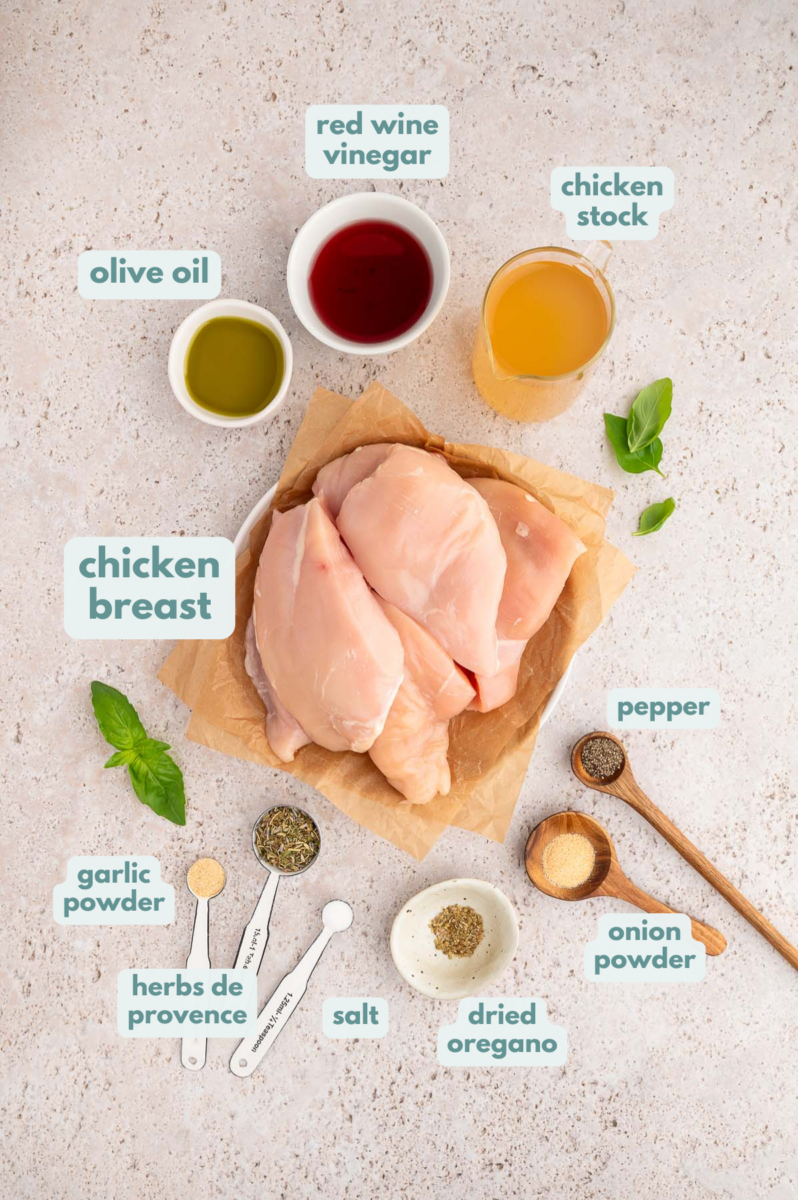 Ingredients for greek shredded chicken in small bowls: boneless, skinless chicken breasts, chicken stock, red wine vinegar, extra virgin olive oil, salt, pepper, garlic powder, onion powder, dried oregano, herbs de provence
