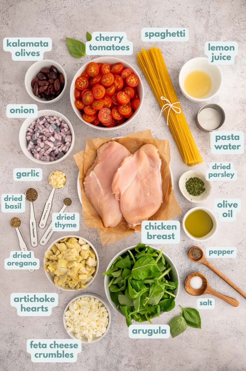 Ingredients for Greek Spaghetti in small bowls: olive oil, boneless, skinless chicken breasts, salt & pepper, onion, garlic, cherry tomatoes, kalamata olives, artichoke hearts, lemon juice, dried oregano, dried parsley, dried basil, dried thyme, spaghetti, arugula, feta cheese