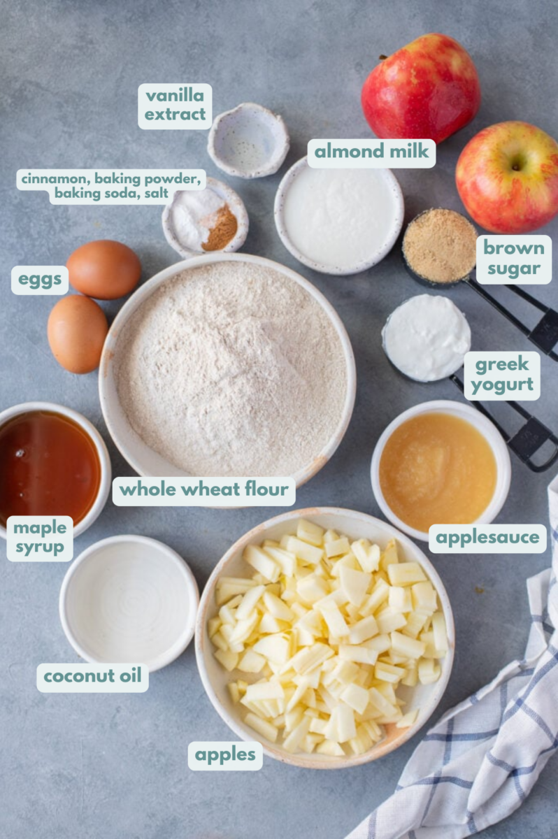 Ingredients for healthy apple muffins laid out on a light grey background in small white bowls.