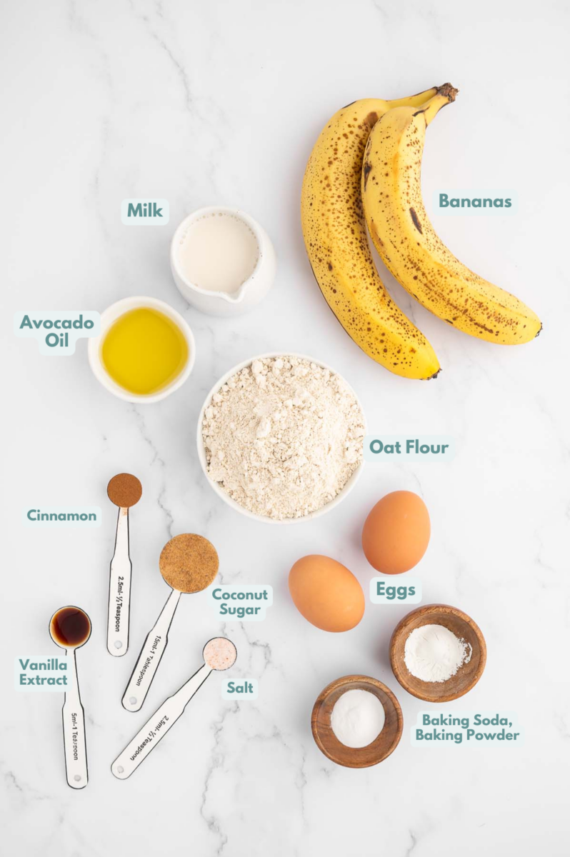 Ingredients for healthy banana pancakes on a marble background: oat flour, coconut sugar, baking soda, baking powder, cinnamon, salt, bananas, milk, eggs, avocado oil, vanilla extract
