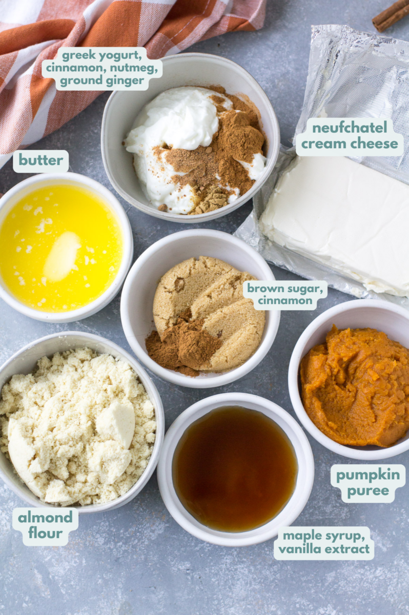 Ingredients for Healthy Pumpkin Cheesecakes in small white bowls: brown sugar, spices, almond flour, butter, pumpkin puree, maple syrup.