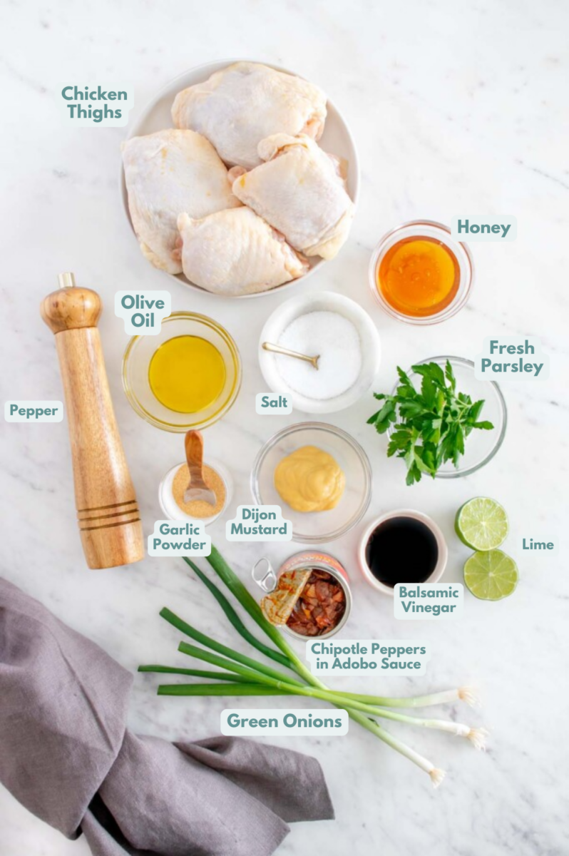 Ingredients for honey chipotle chicken in small bowls: chicken thighs, salt, pepper, paprika, garlic powder, olive oil, honey, chipotle peppers in adobo sauce, dijon mustard, balsamic vinegar, lime, green onions, fresh parsley