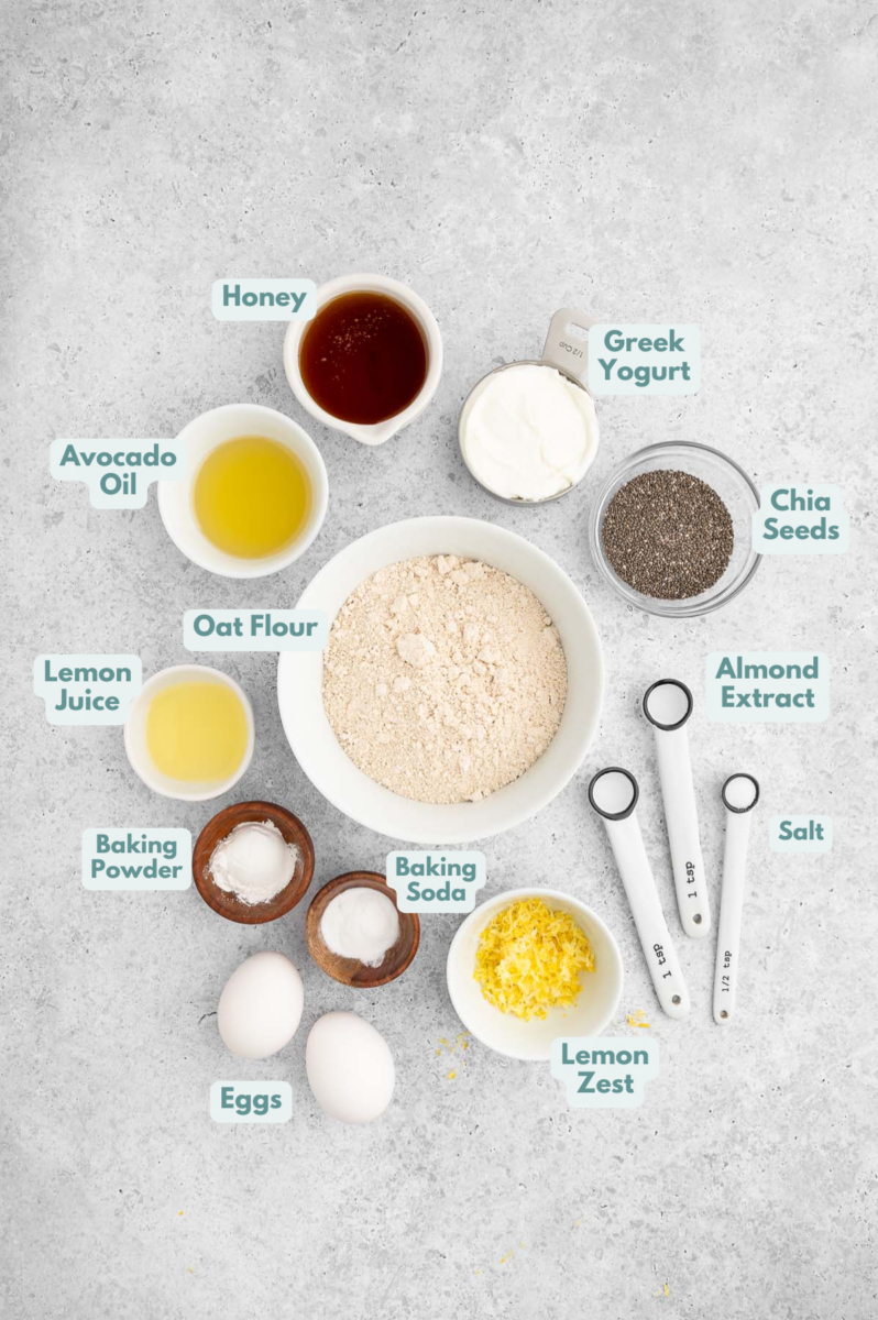 Ingredients for lemon chia muffins in small bowls: honey, Greek yogurt, eggs, avocado oil, lemon zest & lemon juice, lemon extract, almond extract, oat flour, baking powder + baking soda, salt, black chia seeds