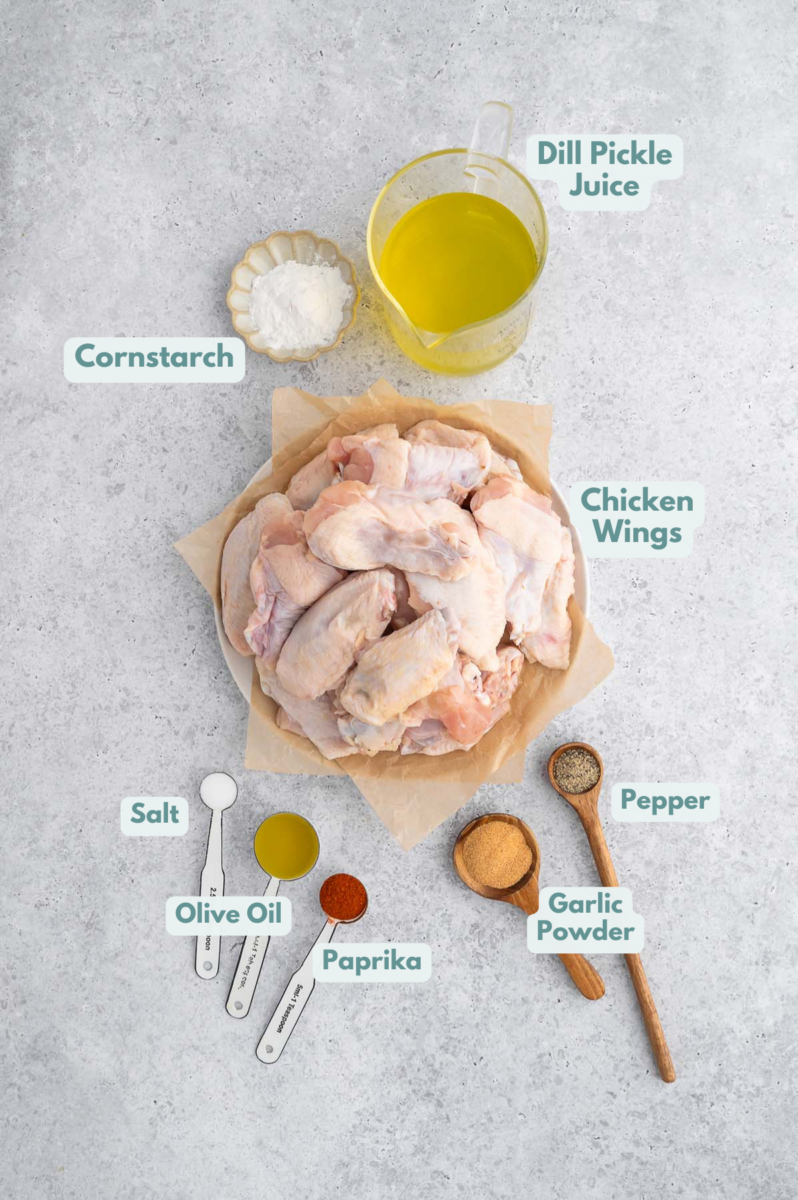 Ingredients for pickle chicken wings in small bowls: chicken wings, dill pickle juice, cornstarch, olive oil, salt, pepper, paprika, garlic powder.