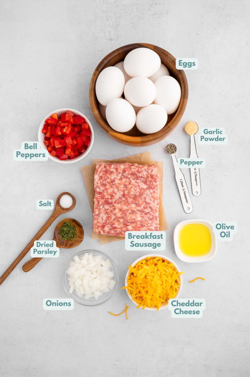 Ingredients for Sausage egg muffins in small bowls: olive oil, breakfast sausage, bell peppers, onion, eggs, garlic powder, pepper, dried parsley, salt, cheddar cheese