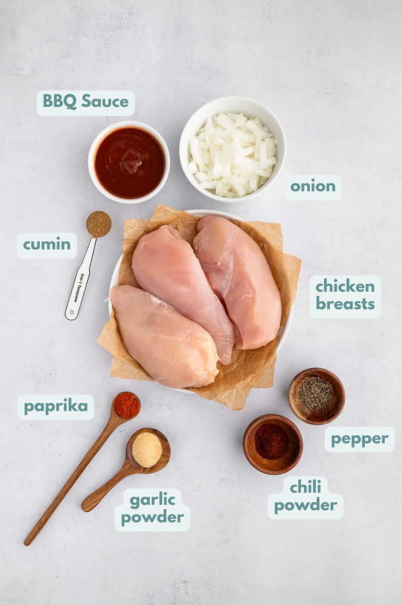 Ingredients for Slow Cooker BBQ Chicken in small containers: boneless, skinless chicken breasts, chili powder, cumin, paprika, garlic powder, pepper, BBQ sauce, diced onion