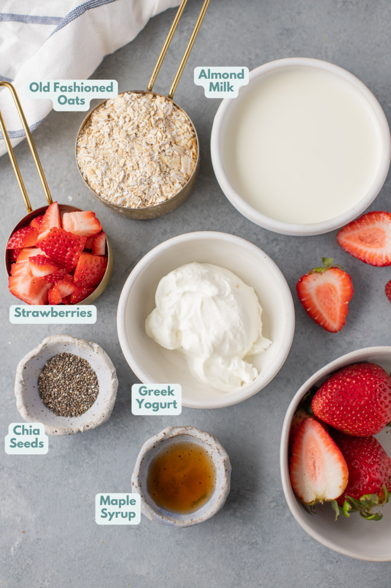 Ingredients for strawberry overnight oats in white bowls: old fashioned rolled oats, nonfat greek yogurt, almond milk, strawberries, maple syrup, chia seeds (optional)