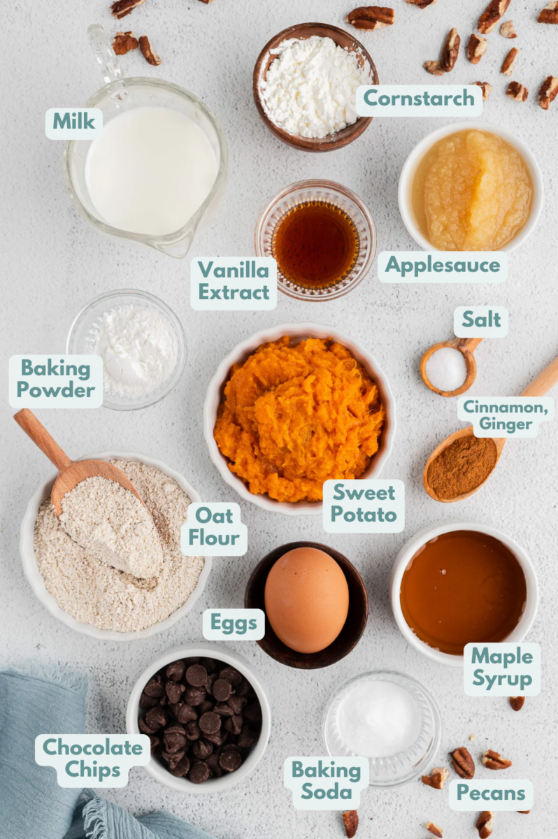 Ingredients for healthy sweet potato muffins in white bowls: mashed sweet potato, applesauce, milk, maple syrup, vanilla extract, oat flour, cornstarch, baking soda, baking powder, salt, ground cinnamon, ground ginger, chopped pecans, chocolate chips.