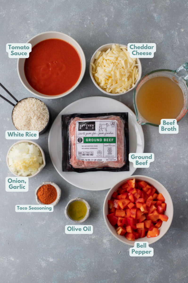 An overhead shot of ingredients for taco skillet in small bowls: olive oil, ground beef, onion, garlic, taco seasoning, tomato sauce, dry white rice, beef broth, bell pepper, shredded cheddar cheese