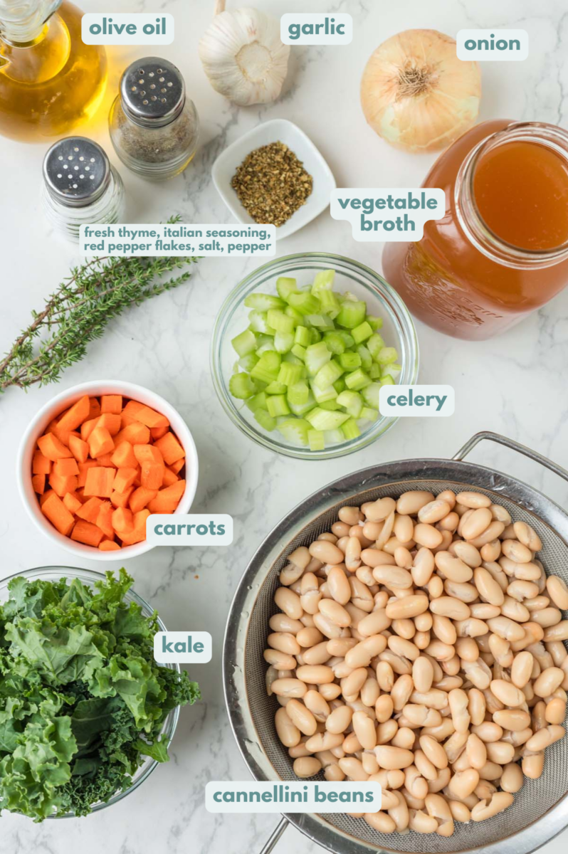 Ingredients for Tuscan white bean soup in small bowls: olive oil, onion, garlic, carrots, celery, Italian seasoning, fresh thyme, salt, pepper, red pepper flakes, cannellini beans, vegetable broth, kale